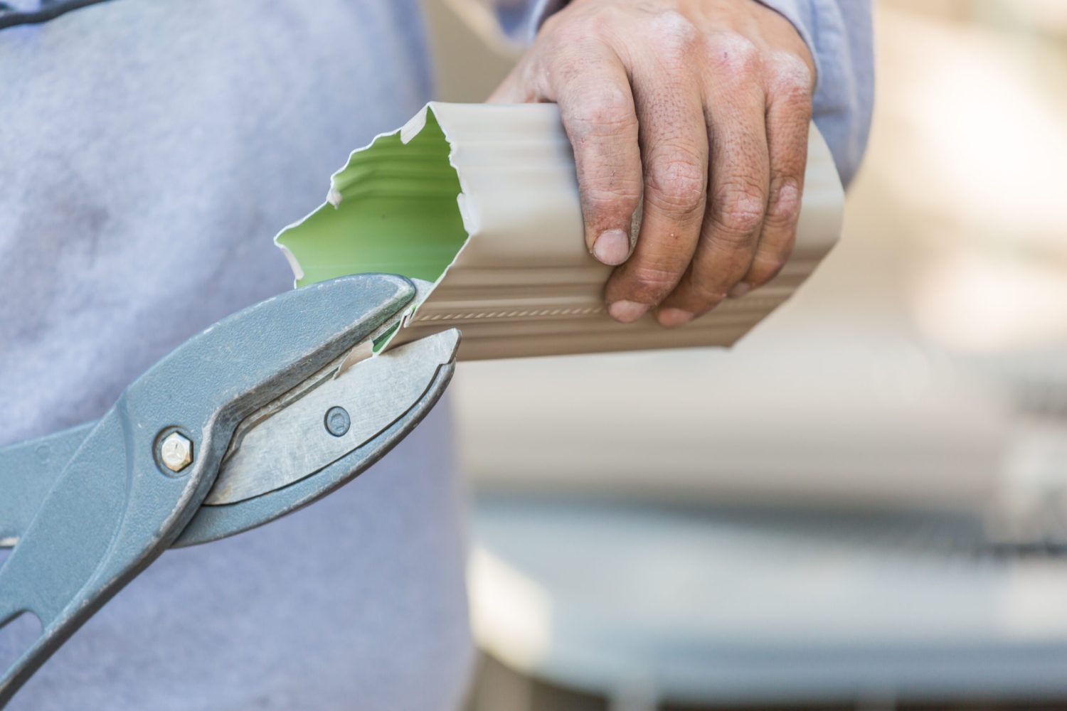 Worker Cutting Aluminum Rain Gutter With Heavy Shears.